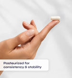 Hand holding a small white pill with text 'Pasteurized for consistency & stability' on a light gray background